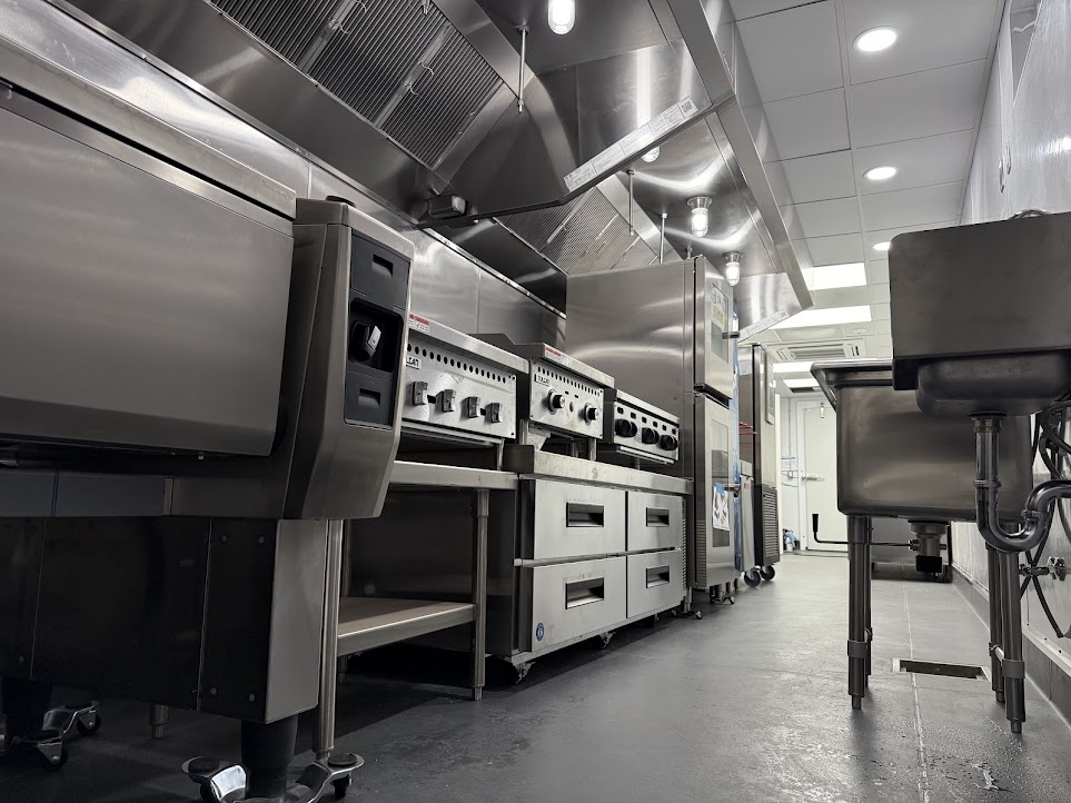 Commercial stainless steel kitchen equipment setup featuring industrial stoves and a deep sink unit